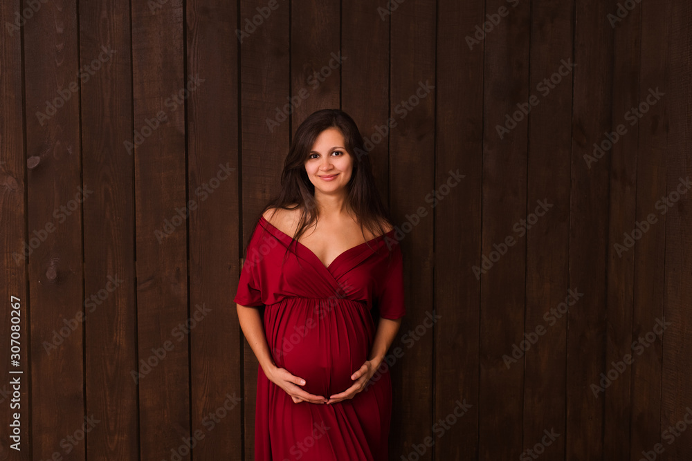 Christmas pregnant woman in red dress holds hands on belly on a dark brown background. Pregnancy, maternity, expectation concept. Beautiful tender mood photo of pregnancy Christmas pregnant woman in red dress holds hands on belly on a dark brown background. Pregnancy, maternity, expectation concept. Beautiful tender mood photo of pregnancy