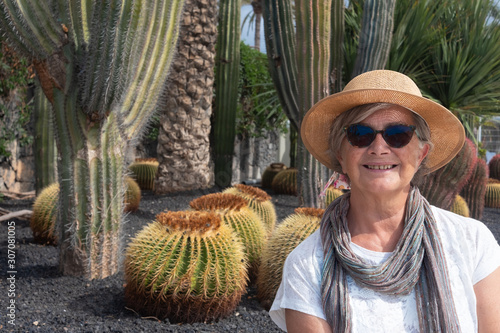 A senior attractive woman with straw hat sitting in the garden with cactus plants around her.