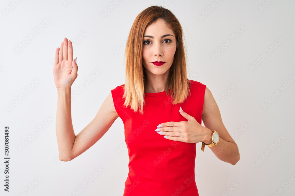 Fototapeta premium Redhead businesswoman wearing elegant red dress standing over isolated white background Swearing with hand on chest and open palm, making a loyalty promise oath