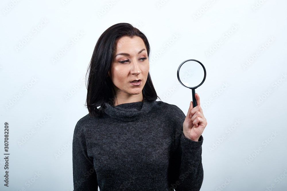 Disappointed caucasian young woman in fashion black sweater over isolated white background, holding magnifier glass. Lifestyle concept Disappointed caucasian young woman in fashion black sweater over isolated white background, holding magnifier glass. Lifestyle concept