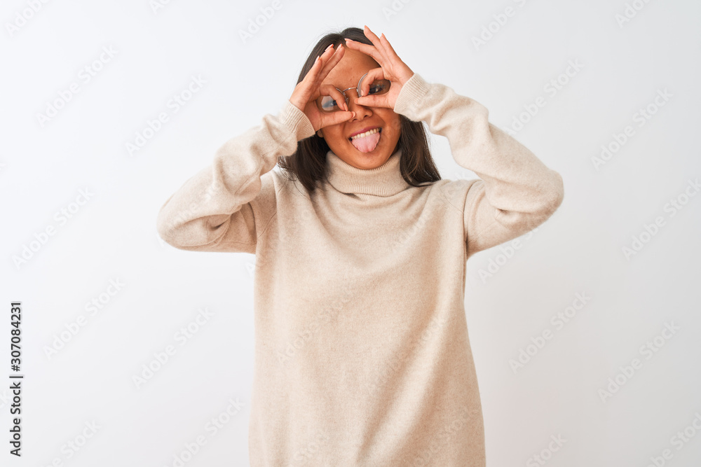 Young chinese woman wearing turtleneck sweater and glasses over isolated white background doing ok gesture like binoculars sticking tongue out, eyes looking through fingers. Crazy expression. Young chinese woman wearing turtleneck sweater and glasses over isolated white background doing ok gesture like binoculars sticking tongue out, eyes looking through fingers. Crazy expression.