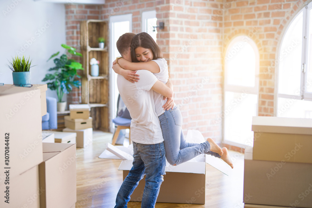Young beautiful couple hugging at new home around cardboard boxes Young beautiful couple hugging at new home around cardboard boxes