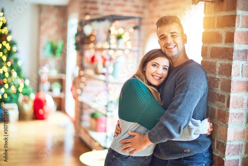 Young beautiful couple smiling happy and confident. Standing and hugging around christmas tree at home