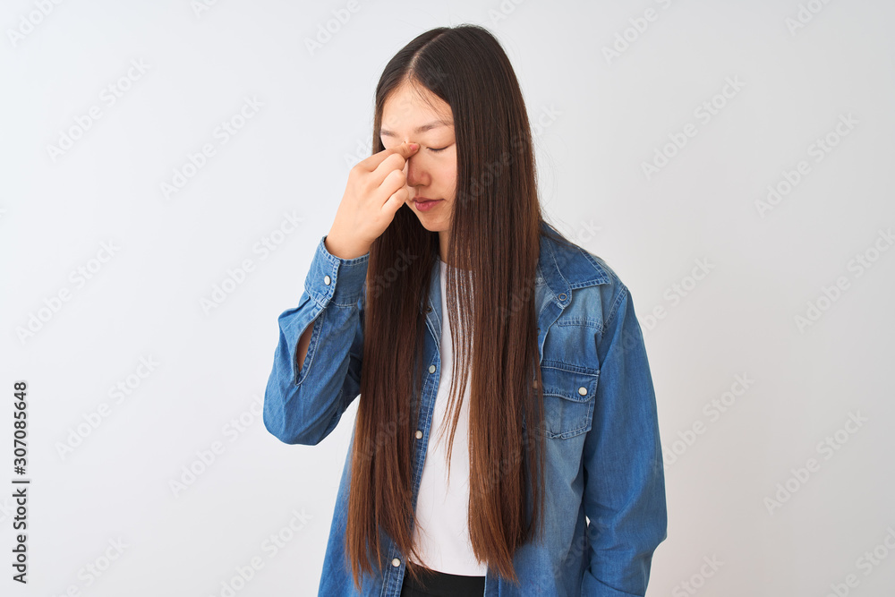 Young chinese woman wearing denim shirt standing over isolated white background tired rubbing nose and eyes feeling fatigue and headache. Stress and frustration concept. Young chinese woman wearing denim shirt standing over isolated white background tired rubbing nose and eyes feeling fatigue and headache. Stress and frustration concept.