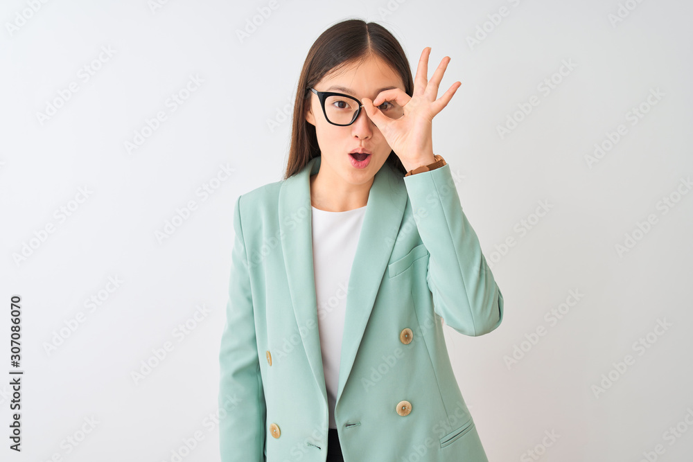 Chinese businesswoman wearing elegant jacket and glasses over isolated white background doing ok gesture shocked with surprised face, eye looking through fingers. Unbelieving expression. Chinese businesswoman wearing elegant jacket and glasses over isolated white background doing ok gesture shocked with surprised face, eye looking through fingers. Unbelieving expression.