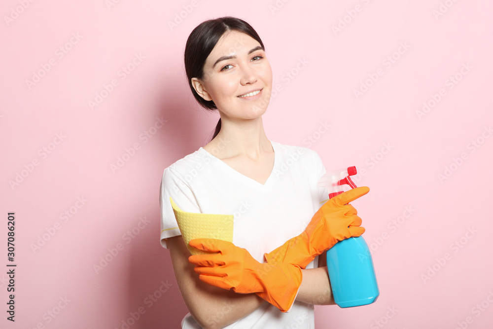 A young housewife holds in his hands cleaning products on a colored background. A young housewife holds in his hands cleaning products on a colored background.