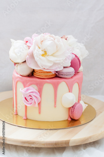 White cake with pink melted chocolate  fresh roses and peonies  macaroons and meringues. 