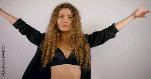 Portrait of a smiling curly-haired girl who is in the Studio on a white background, wearing a black unbuttoned jacket and a black bra, she poses and touches her hair.