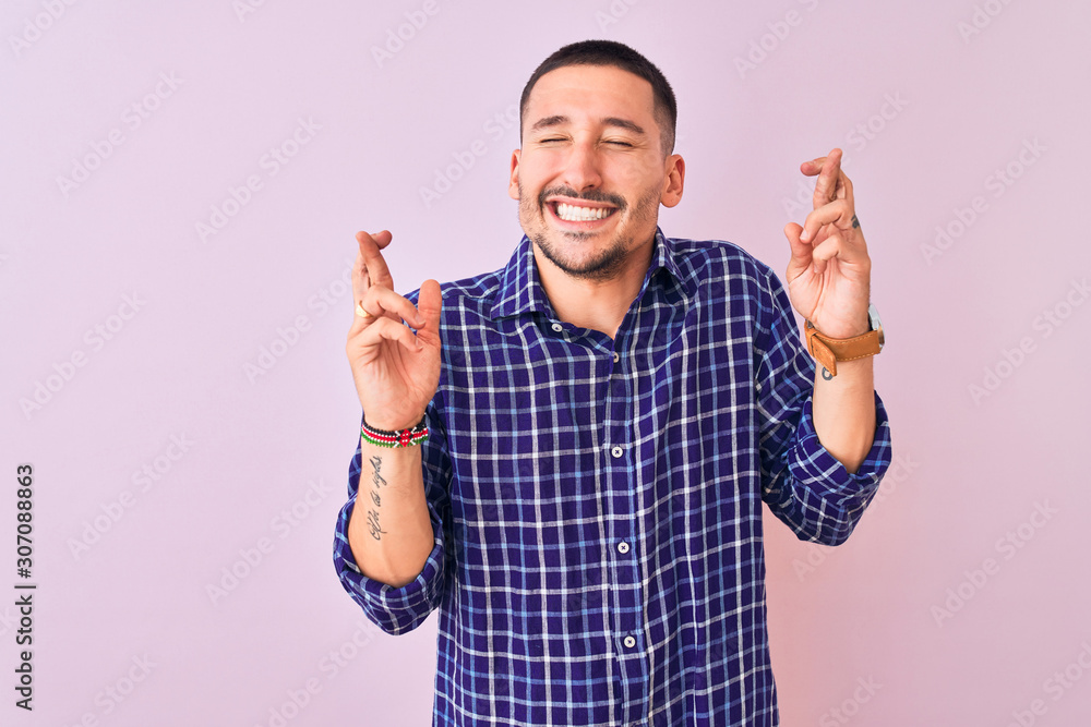 Young handsome man standing over isolated background gesturing finger crossed smiling with hope and eyes closed. Luck and superstitious concept. Young handsome man standing over isolated background gesturing finger crossed smiling with hope and eyes closed. Luck and superstitious concept.