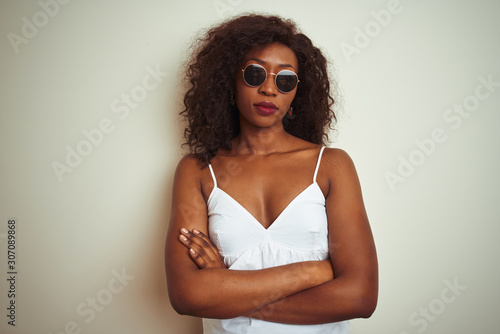 Young african american woman wearing t-shirt and sunglasses over isolated white background skeptic and nervous, disapproving expression on face with crossed arms. Negative person.
