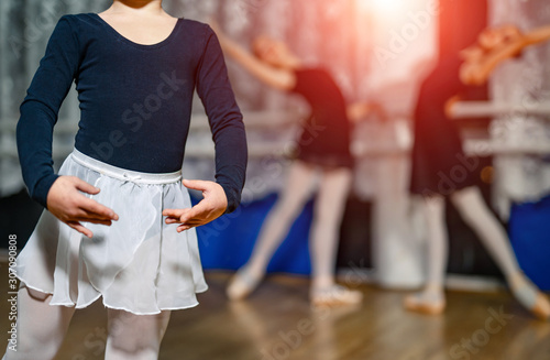 Cute little ballerina in dance studio posing and training with ballet team in the background. Selective focus. Closeup.