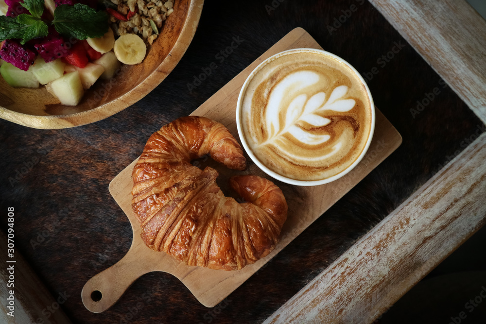 A cup of coffee with latte art on top, butter croissant and granola with fresh tropical fruits and yogurt on table in caffee, top view. Concept of healthy breakfast A cup of coffee with latte art on top, butter croissant and granola with fresh tropical fruits and yogurt on table in caffee, top view. Concept of healthy breakfast