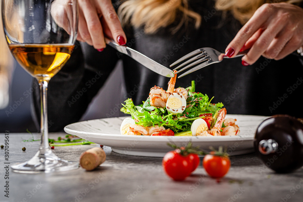 Girl in a restaurant eating Caesar salad with seafood and shrimp. A glass of white wine on the table. Modern serve in a restaurant. Background image. Copy space Girl in a restaurant eating Caesar salad with seafood and shrimp. A glass of white wine on the table. Modern serve in a restaurant. Background image. Copy space