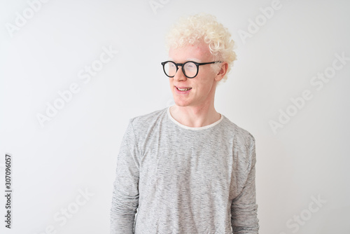 Young albino blond man wearing striped t-shirt and glasses over isolated white background looking away to side with smile on face, natural expression. Laughing confident.