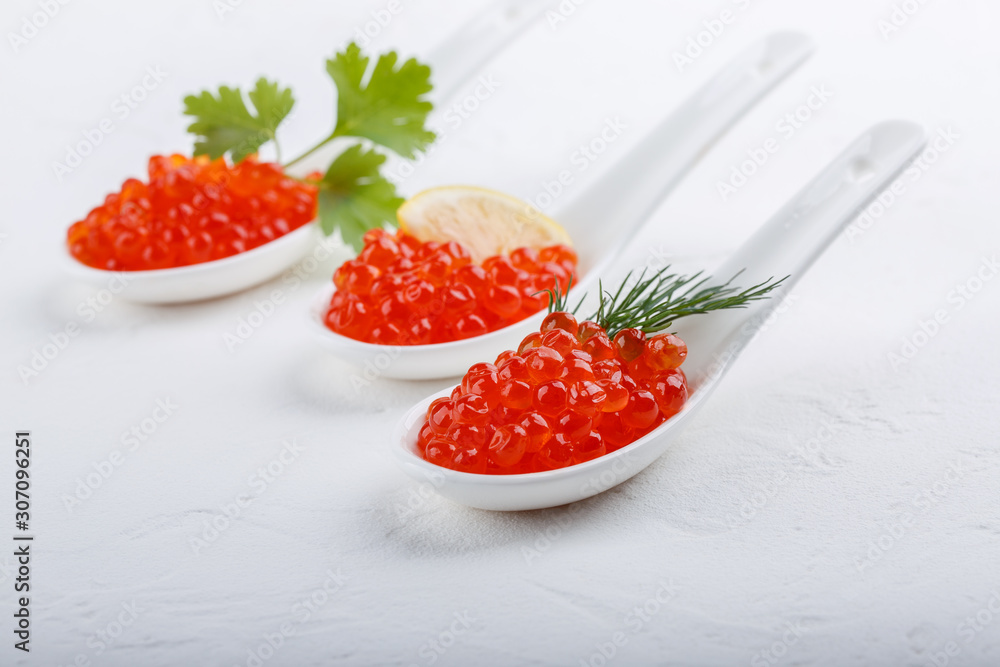 Red caviar in ceramic spoons on white background. Close-up, copy space. Red caviar in ceramic spoons on white background. Close-up, copy space.