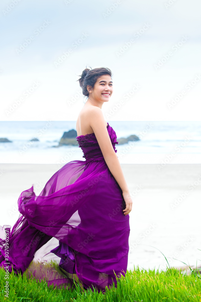 Teen girl wearing purple gown on grassy knoll overlooking ocean Teen girl wearing purple gown on grassy knoll overlooking ocean