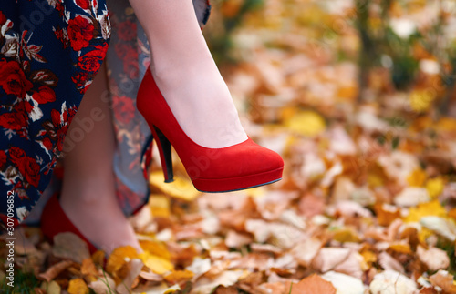 close up of women's feet shod in red high heels shoes, autumn season, yellow fallen leaves as background