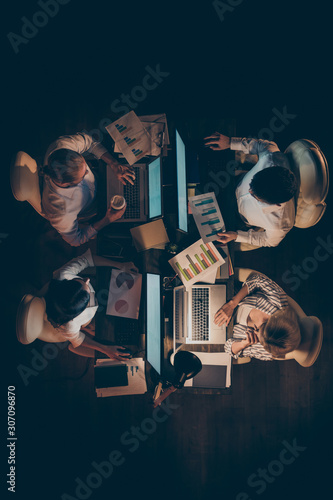 Vertical top above high angle view of four hardworking entrepreneurs IT experienced skilled managers creating web design coding preparing report at late night workplace workstation