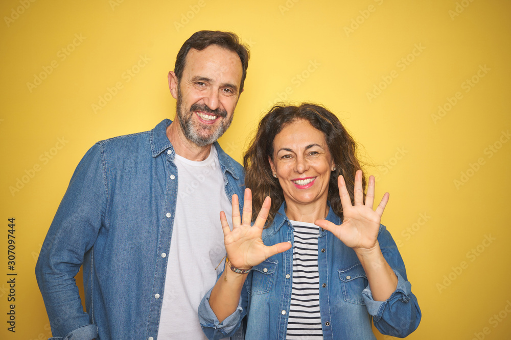 Beautiful middle age couple together wearing denim shirt over isolated yellow background showing and pointing up with fingers number ten while smiling confident and happy. Beautiful middle age couple together wearing denim shirt over isolated yellow background showing and pointing up with fingers number ten while smiling confident and happy.