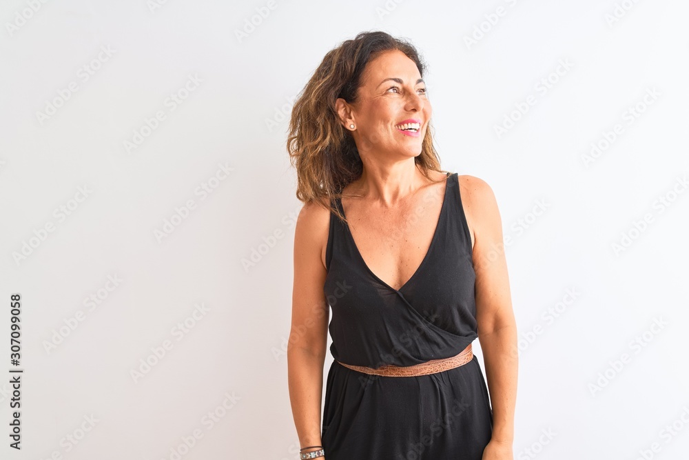 Middle age woman wearing black casual dress standing over isolated white background looking away to side with smile on face, natural expression. Laughing confident. Middle age woman wearing black casual dress standing over isolated white background looking away to side with smile on face, natural expression. Laughing confident.