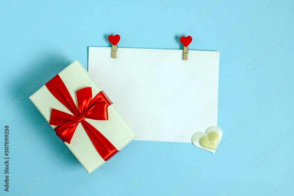 Valentines day flat lay copy space. On a blue background is a white sheet of paper held by two rags decorated with red hearts. Near the leader in the box.Background for a declaration of love Valentines day flat lay copy space. On a blue background is a white sheet of paper held by two rags decorated with red hearts. Near the leader in the box.Background for a declaration of love