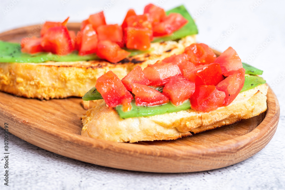 two Italian bruschettes with cheese and tomatoes on a wooden plate