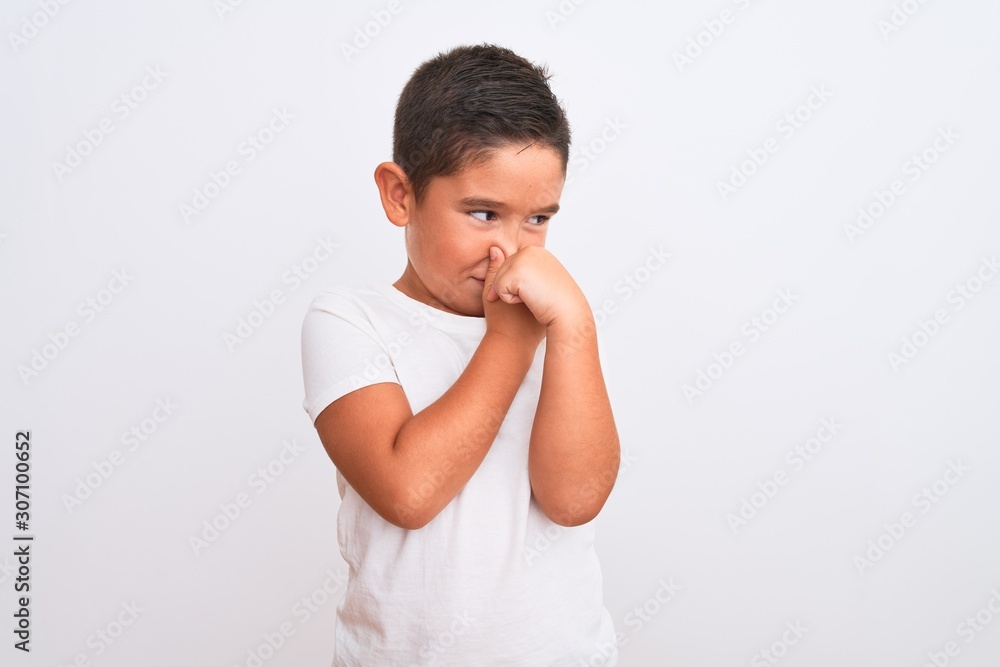 Beautiful kid boy wearing casual t-shirt standing over isolated white background smelling something stinky and disgusting, intolerable smell, holding breath with fingers on nose. Bad smells concept. Beautiful kid boy wearing casual t-shirt standing over isolated white background smelling something stinky and disgusting, intolerable smell, holding breath with fingers on nose. Bad smells concept.