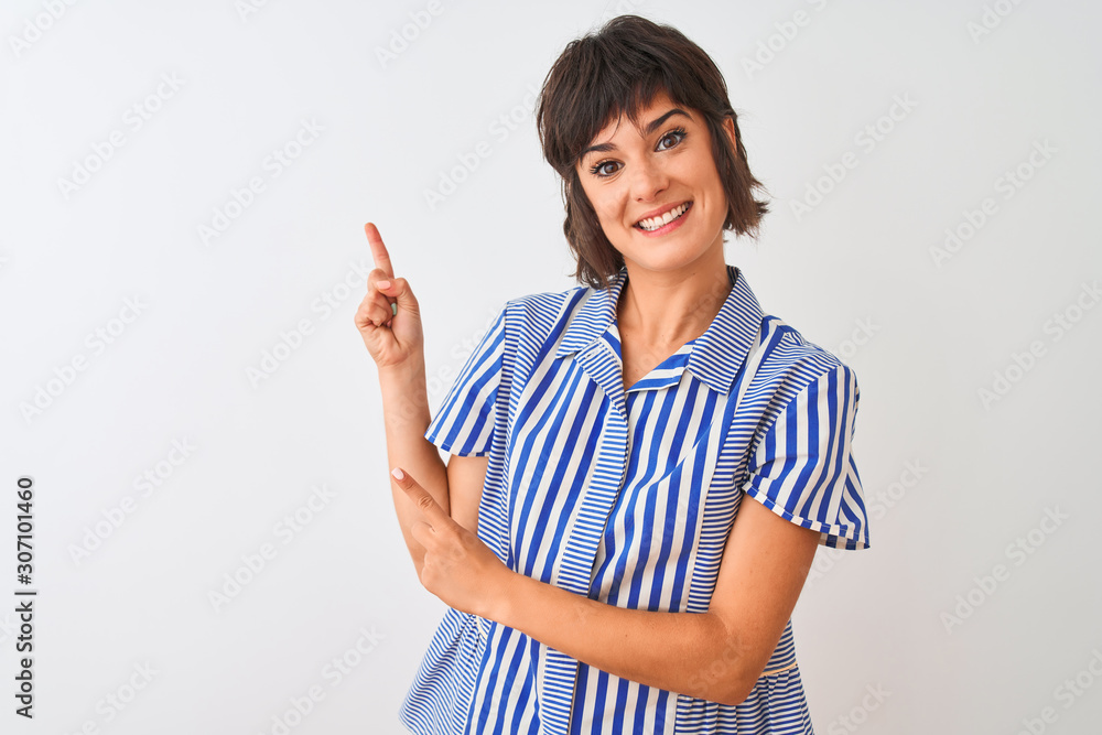 Young beautiful woman wearing blue striped shirt standing over isolated white background smiling and looking at the camera pointing with two hands and fingers to the side. Young beautiful woman wearing blue striped shirt standing over isolated white background smiling and looking at the camera pointing with two hands and fingers to the side.
