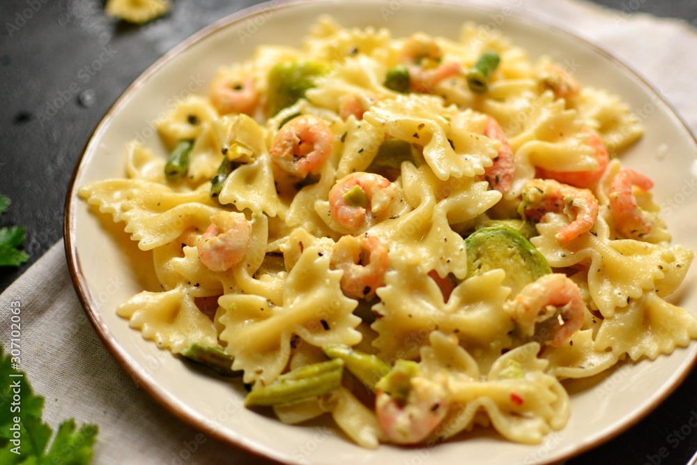 Italian pasta in a creamy sauce with shrimp on a plate, top view. Pasta in the form of bows on a dark table background. Italian pasta in a creamy sauce with shrimp on a plate, top view. Pasta in the form of bows on a dark table background.