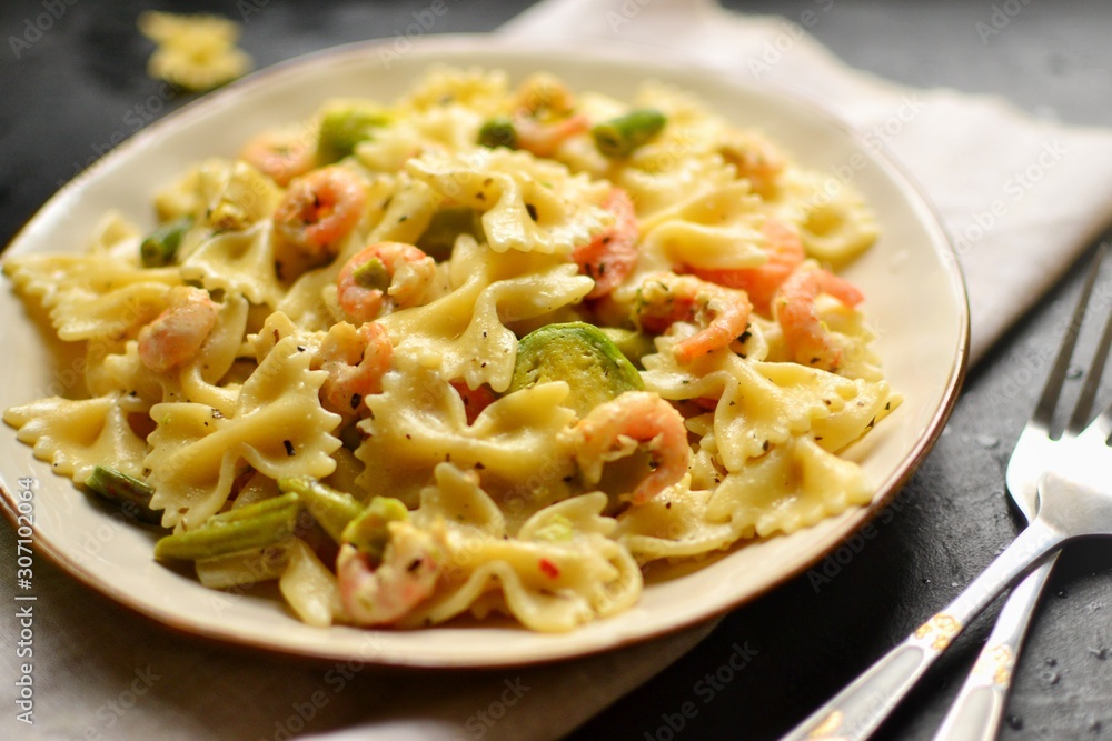 Italian pasta in a creamy sauce with shrimp on a plate, top view. Pasta in the form of bows on a dark table background. Italian pasta in a creamy sauce with shrimp on a plate, top view. Pasta in the form of bows on a dark table background.