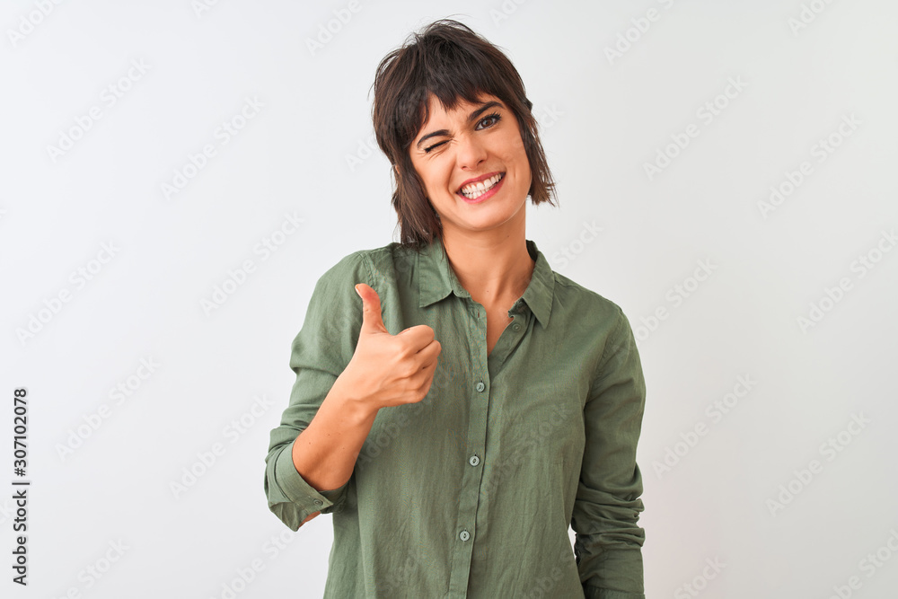 Young beautiful woman wearing green casual shirt standing over isolated white background doing happy thumbs up gesture with hand. Approving expression looking at the camera with showing success. Young beautiful woman wearing green casual shirt standing over isolated white background doing happy thumbs up gesture with hand. Approving expression looking at the camera with showing success.