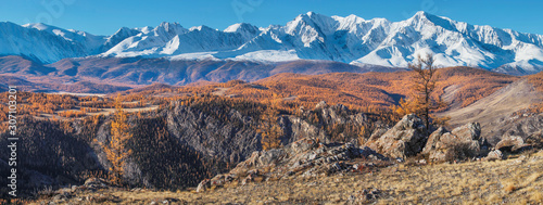 Panoramic autumn view, sunny day. Picturesque mountain landscape. Snow-capped peaks and blue sky.