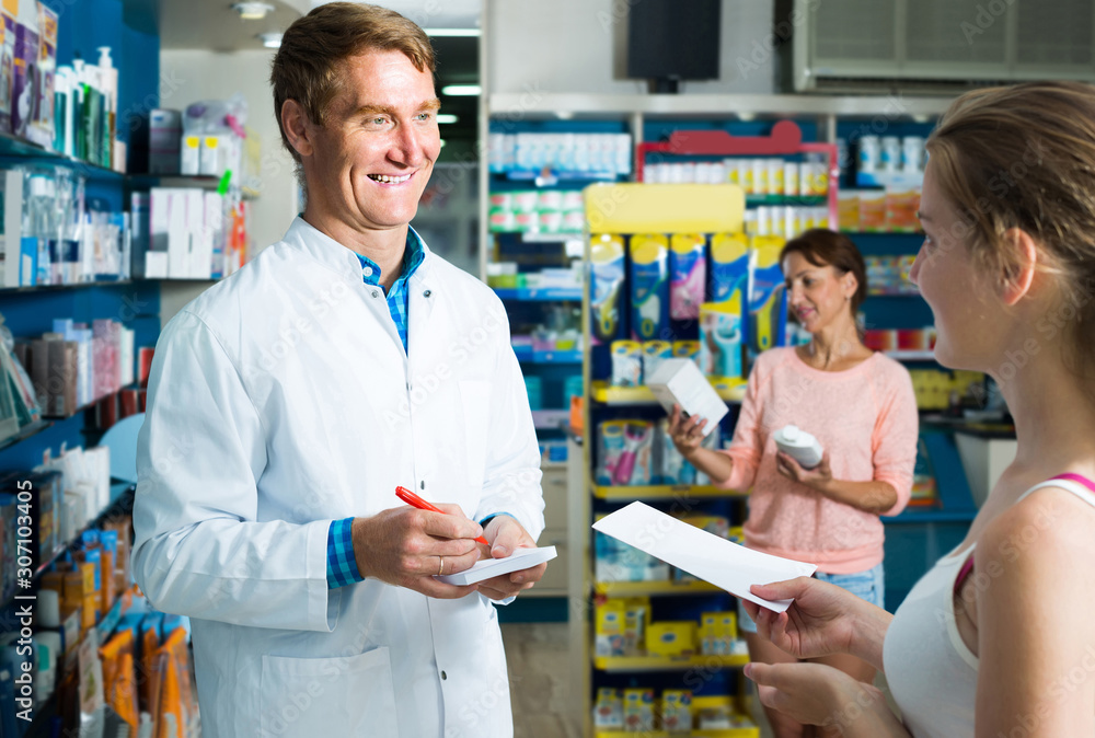 portrait of man druggist in white coat giving advice to customers in pharmacy