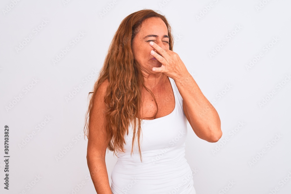 Middle age mature woman standing over white isolated background smelling something stinky and disgusting, intolerable smell, holding breath with fingers on nose. Bad smells concept. Middle age mature woman standing over white isolated background smelling something stinky and disgusting, intolerable smell, holding breath with fingers on nose. Bad smells concept.