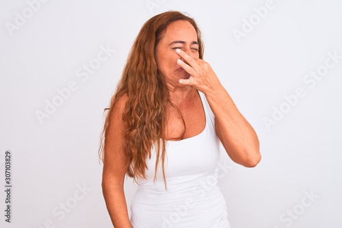 Middle age mature woman standing over white isolated background smelling something stinky and disgusting, intolerable smell, holding breath with fingers on nose. Bad smells concept.