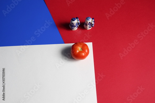 Salt and pepper ceramic castors and fresh tomato on white, blue, red colored background photo