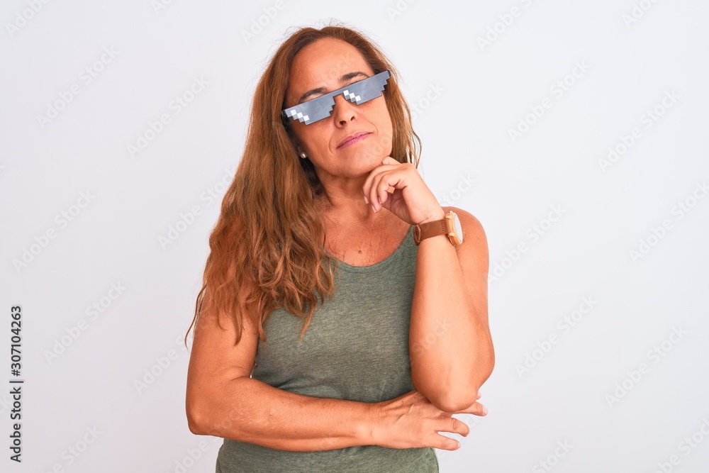 Middle age mature woman wearing thug life sunglasses over isolated background with hand on chin thinking about question, pensive expression. Smiling with thoughtful face. Doubt concept. Middle age mature woman wearing thug life sunglasses over isolated background with hand on chin thinking about question, pensive expression. Smiling with thoughtful face. Doubt concept.