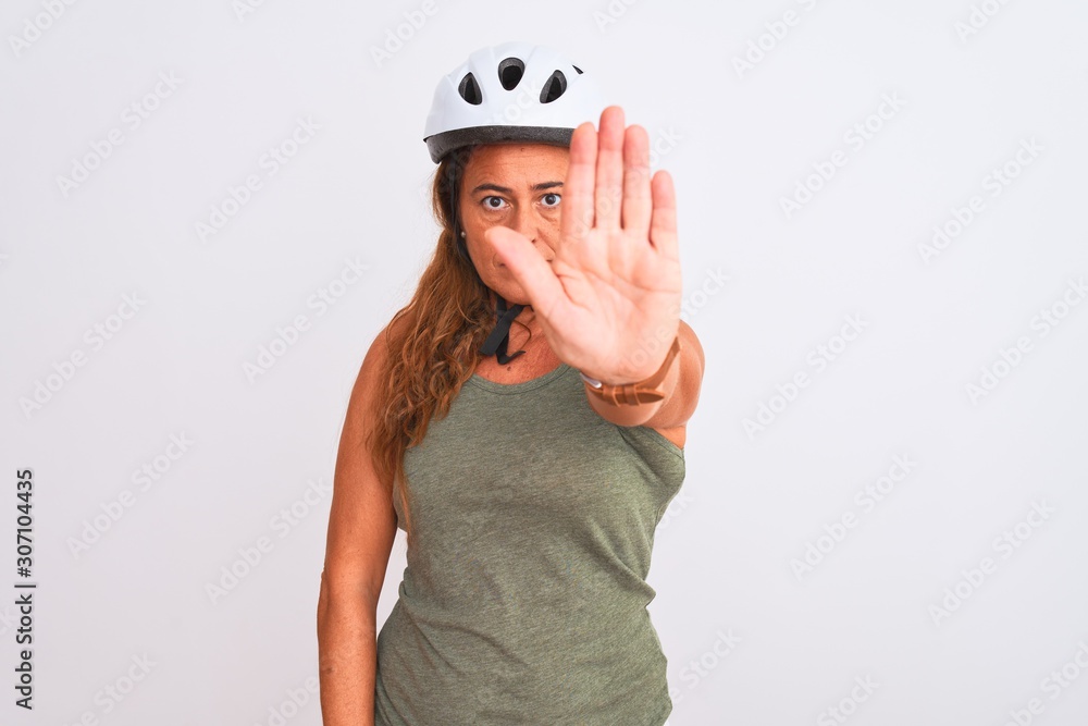 Middle age mature cyclist woman wearing safety helmet over isolated background doing stop sing with palm of the hand. Warning expression with negative and serious gesture on the face. Middle age mature cyclist woman wearing safety helmet over isolated background doing stop sing with palm of the hand. Warning expression with negative and serious gesture on the face.