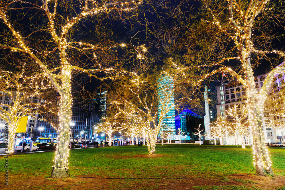 Obraz premium Festive decoration in city Berlin in Germany on December on Christmas and New Year winter holidays. Decorated with illuminated lamp garland trees on Potsdamer Platz in Berlin. 