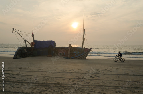 Silhouette of a cyclist on bicycle passing by a ship wreck during sunset at the beach of goa India