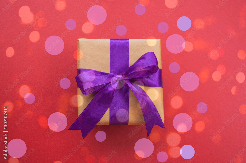 Giftbox tied with purple color ribbon on dark red background with beautiful confetti. Flat lay style. Giftbox tied with purple color ribbon on dark red background with beautiful confetti. Flat lay style.