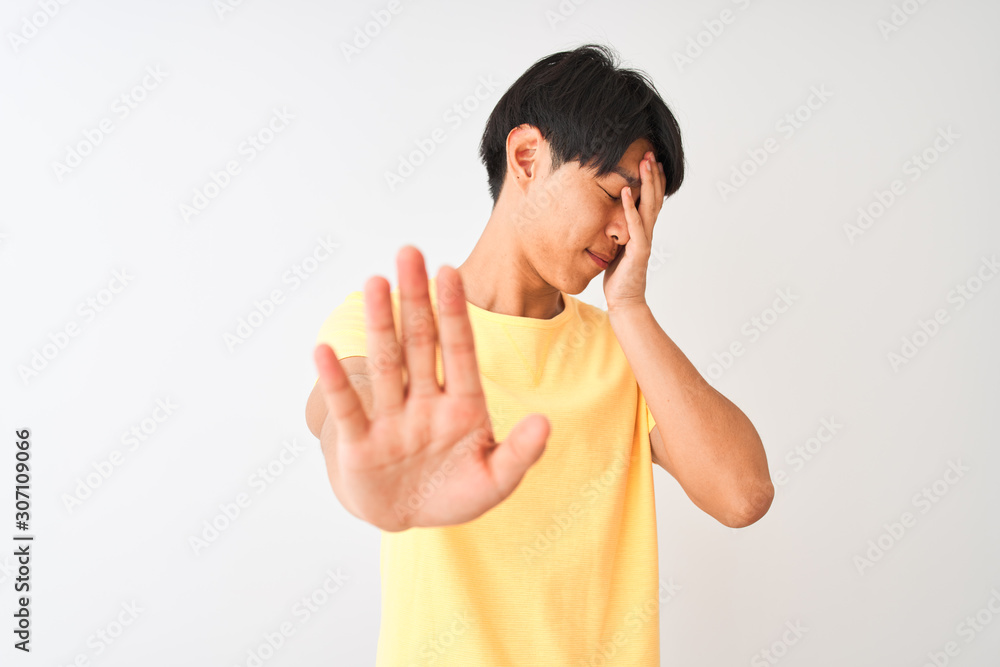 Chinese man wearing yellow casual t-shirt standing over isolated white background covering eyes with hands and doing stop gesture with sad and fear expression. Embarrassed and negative concept. Chinese man wearing yellow casual t-shirt standing over isolated white background covering eyes with hands and doing stop gesture with sad and fear expression. Embarrassed and negative concept.