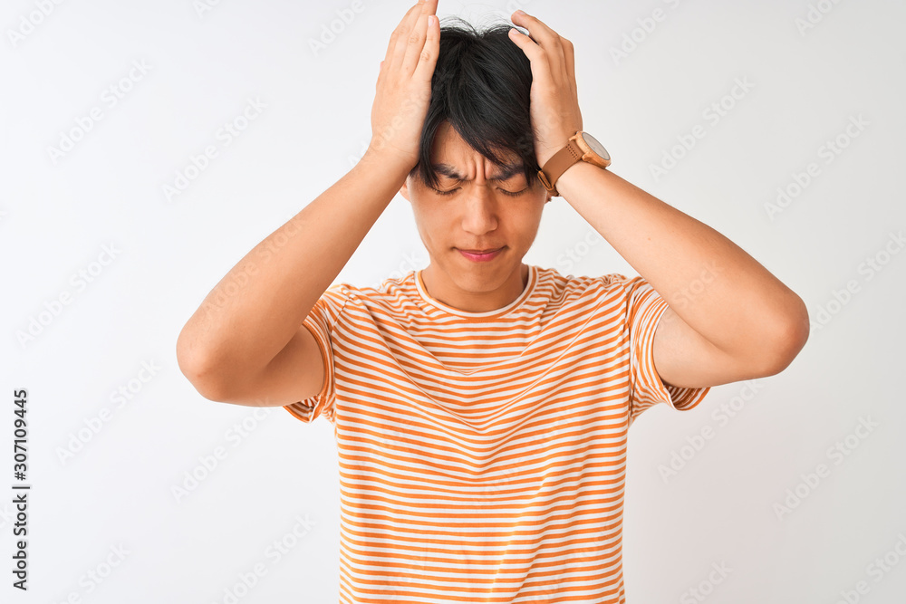 Young chinese man wearing casual striped t-shirt standing over isolated white background suffering from headache desperate and stressed because pain and migraine. Hands on head. Young chinese man wearing casual striped t-shirt standing over isolated white background suffering from headache desperate and stressed because pain and migraine. Hands on head.