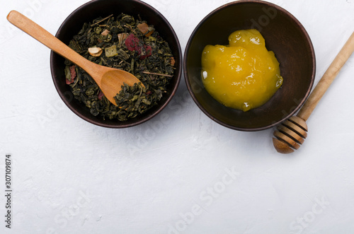 Top view of bowls with sweet hoey, dried green tea with fruits, herbs, wooden spoon adn honey dipper on the white table.Free space for text photo