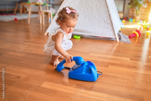 Beautiful caucasian infant playing with toys at colorful playroom. Happy and playful calling with vitange telephone at kindergarten.