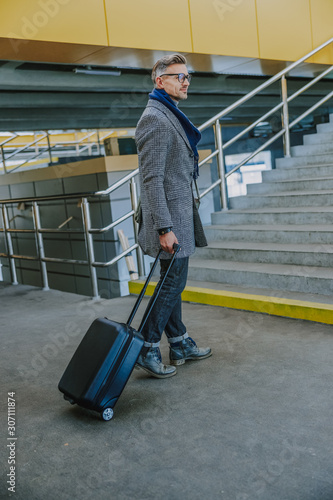 Handsome stylish man carrying travel suitcase at railway station