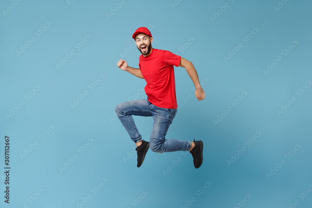 Obraz premium Delivery man in red uniform workwear isolated on blue wall background, studio portrait. Professional male employee in cap t-shirt print working as courier dealer. Service concept. Mock up copy space.