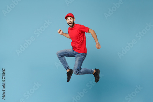 Delivery man in red uniform workwear isolated on blue wall background, studio portrait. Professional male employee in cap t-shirt print working as courier dealer. Service concept. Mock up copy space.