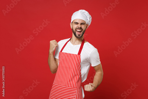 Slika na platnu Joyful bearded male chef cook or baker man in striped apron white t-shirt toque chefs hat posing isolated on red background