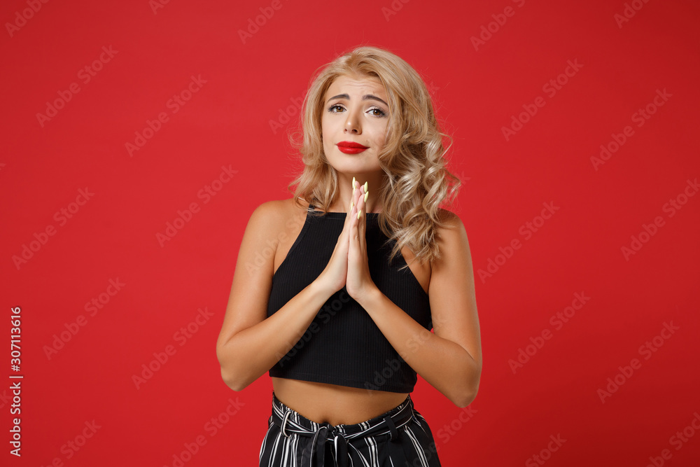 Pleading young woman girl in black clothes posing isolated on bright red wall background studio portrait. People sincere emotions lifestyle concept. Mock up copy space. Holding hands folded in prayer. Pleading young woman girl in black clothes posing isolated on bright red wall background studio portrait. People sincere emotions lifestyle concept. Mock up copy space. Holding hands folded in prayer.